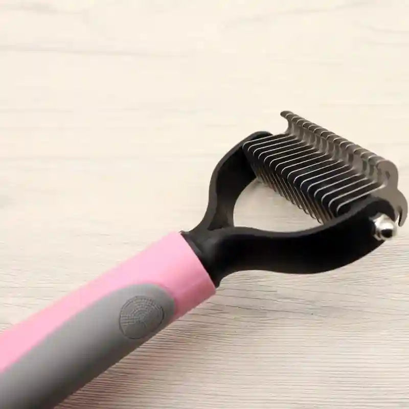 Double-sided dematting comb with wide and narrow stainless steel blades, pink and gray ergonomic handle.