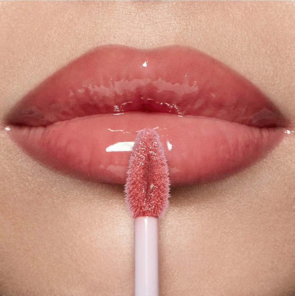 Glossy pink hyaluronic lip gloss applied on smooth lips with applicator wand touching lower lip.