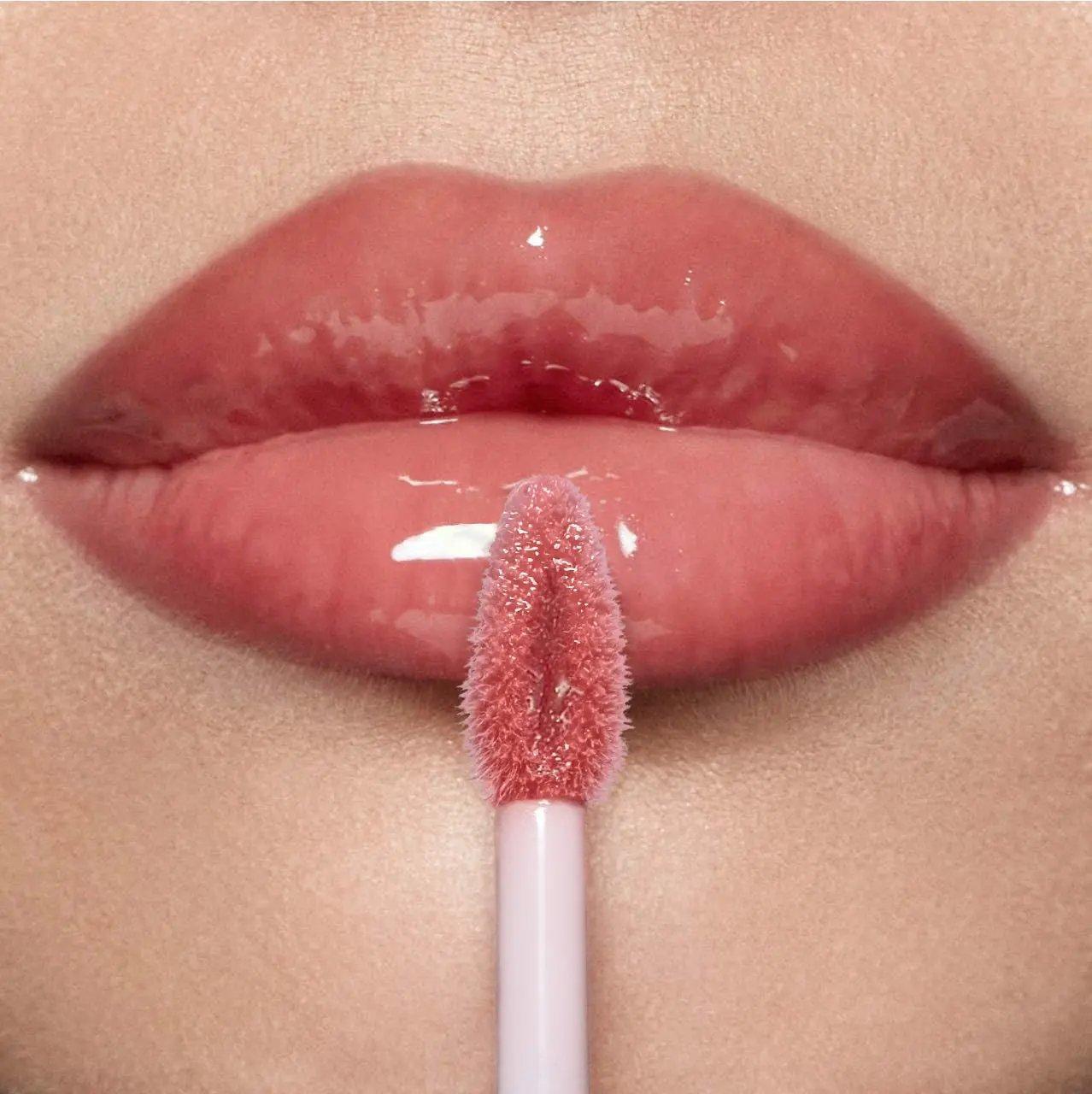 Glossy pink hyaluronic lip gloss applied on smooth lips with applicator wand touching lower lip.